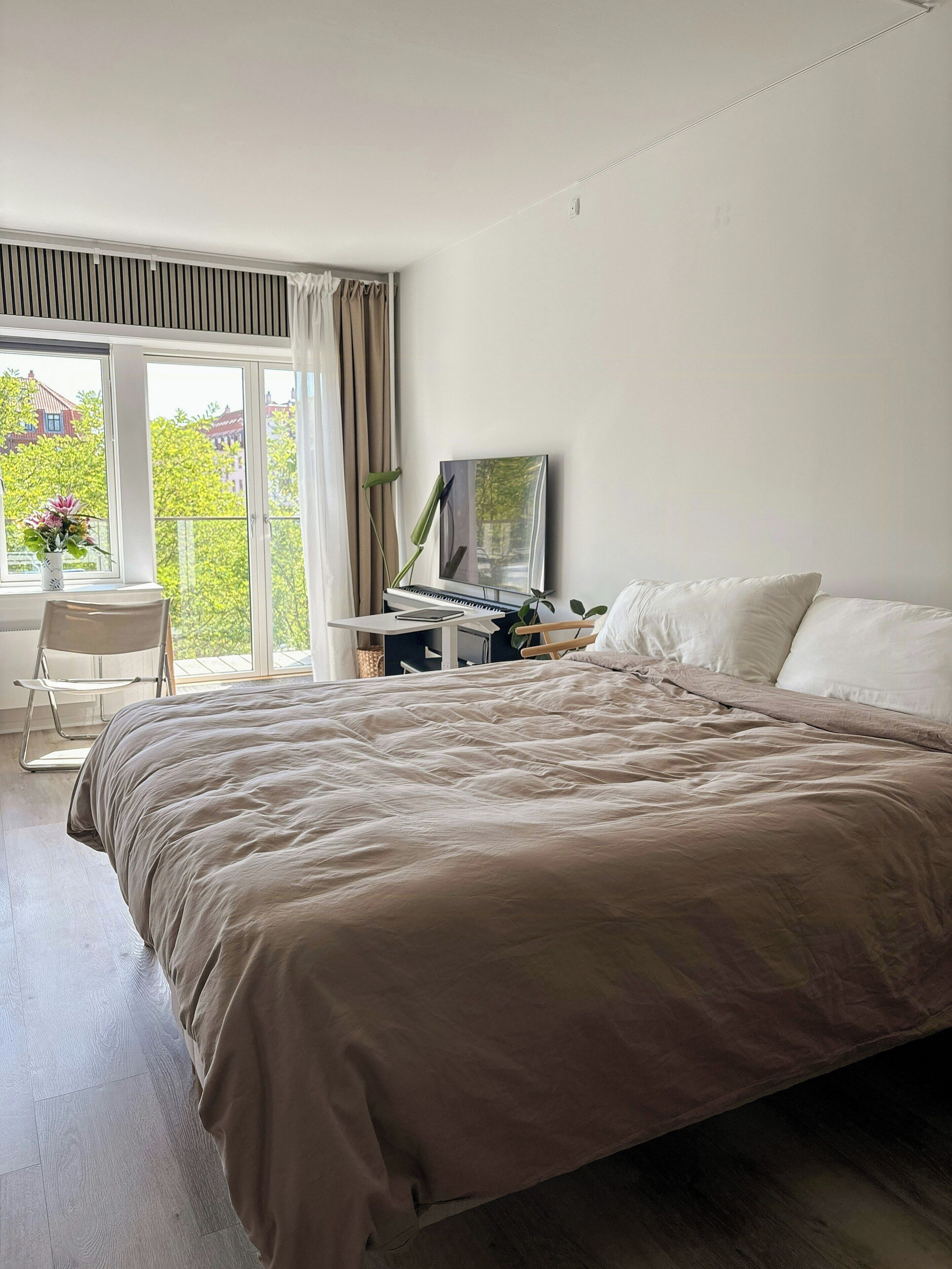 A bedroom with a bed, a desk with a computer, and a window with curtains.
