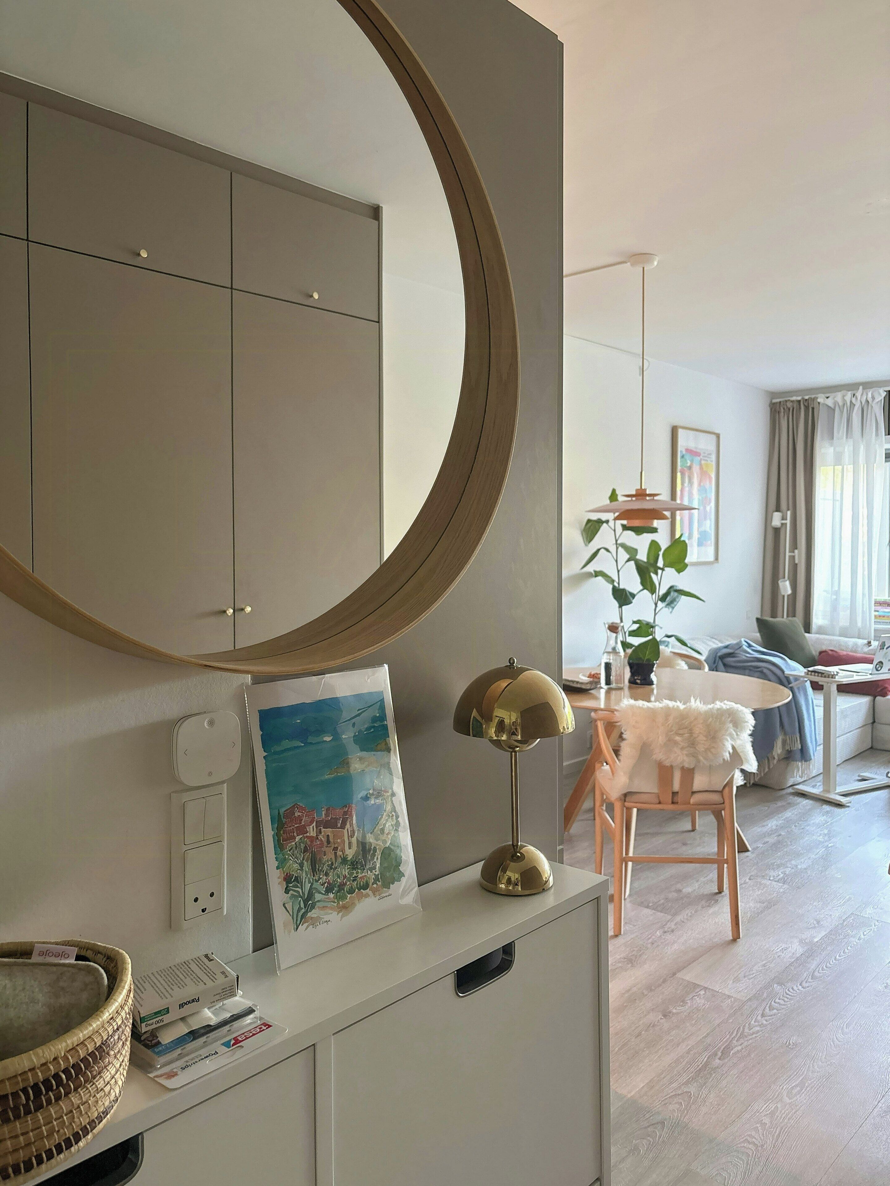 Una habitación luminosa con un espejo grande, un cuadro, una lámpara y un comedor con mesa y sillas.