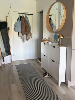 A room with a white wardrobe, a mirror, a standing lamp, and a coat rack with hanging clothes. - Light flat on Islands Brygge with balcony (København)