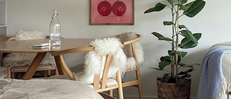 A room with a bed, a wooden chair, a table with a bottle, and a potted plant.