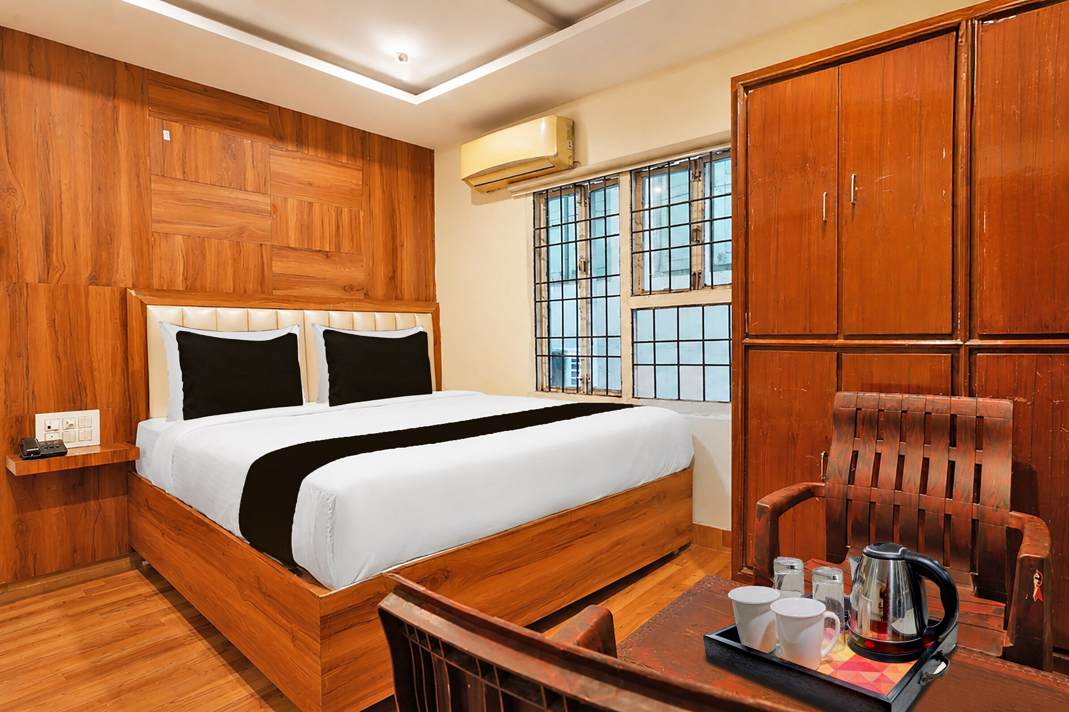 Habitación de hotel con cama de madera, ventana con rejas, armario de madera y una mesa con hervidor y tazas.