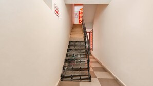Un couloir étroit avec un escalier menant à une porte sur laquelle est apposée une enseigne rouge et blanche.