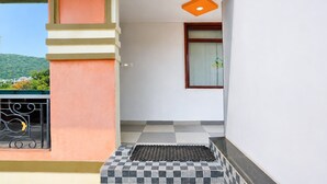 Un balcon avec un sol à carreaux, une fenêtre ornée d’une plante verte et une vue sur une colline verdoyante.