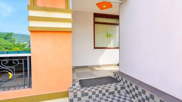 A balcony with a view of greenery, a window with a logo, and a tiled floor.