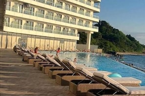 A hotel with a pool area, lounge chairs, and a view of the sea.