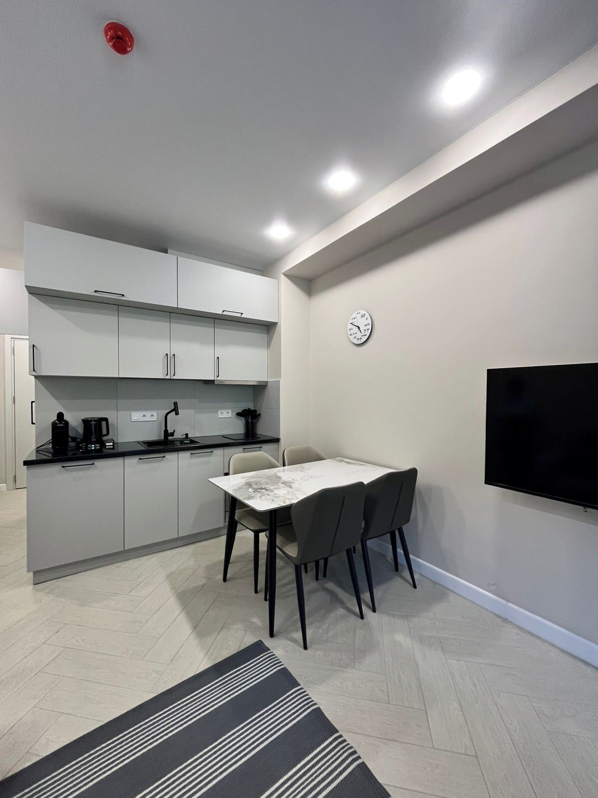 A compact kitchen with modern appliances, a dining area with a table and chairs, and a flat-screen TV mounted on the wall.