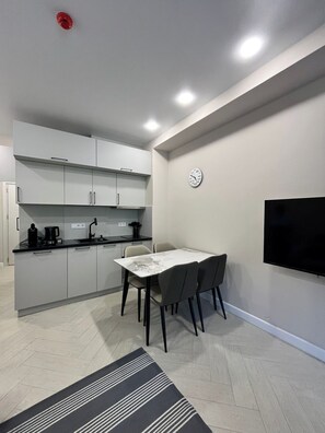 Una cocina funcional con electrodomésticos modernos, un comedor con mesa y sillas, y un televisor de pantalla plana montado en la pared.