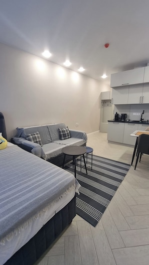 Una habitación moderna y bien iluminada con sofá, una mesita redonda y una zona de kitchenette.