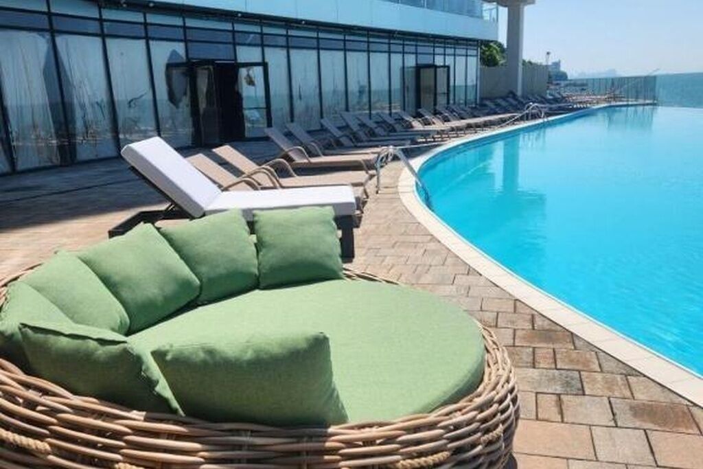 A poolside area with lounge chairs and a wicker chair with cushions.
