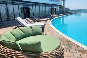 Un espace aménagé au bord de la piscine, avec des chaises longues et un fauteuil en osier doté de coussins.