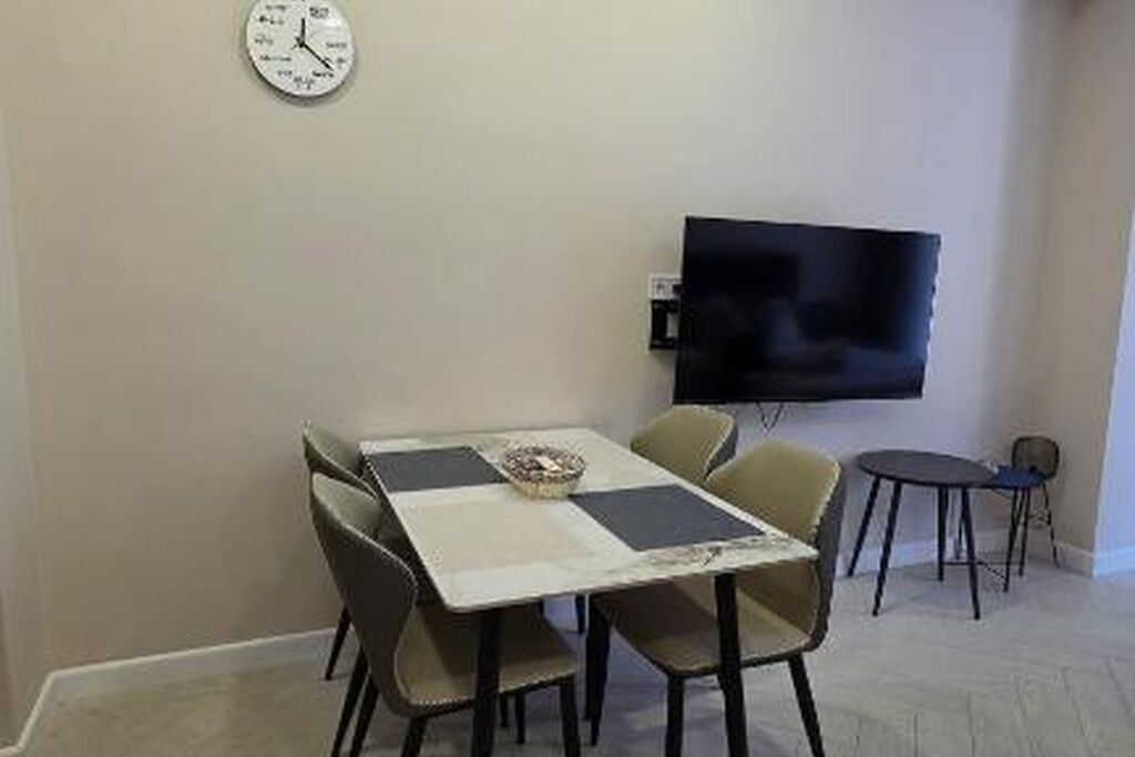 A dining area with a table, chairs, a clock, and a television on the wall.