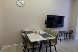 Un coin repas avec une table, des chaises, une horloge et un téléviseur fixé au mur.