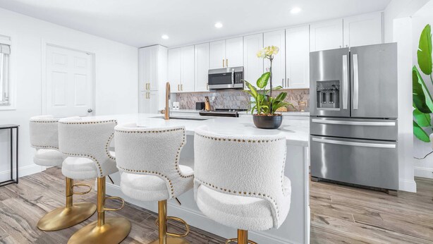 Una cocina moderna con armarios blancos, electrodomésticos de acero inoxidable y una isla central con taburetes de bar.