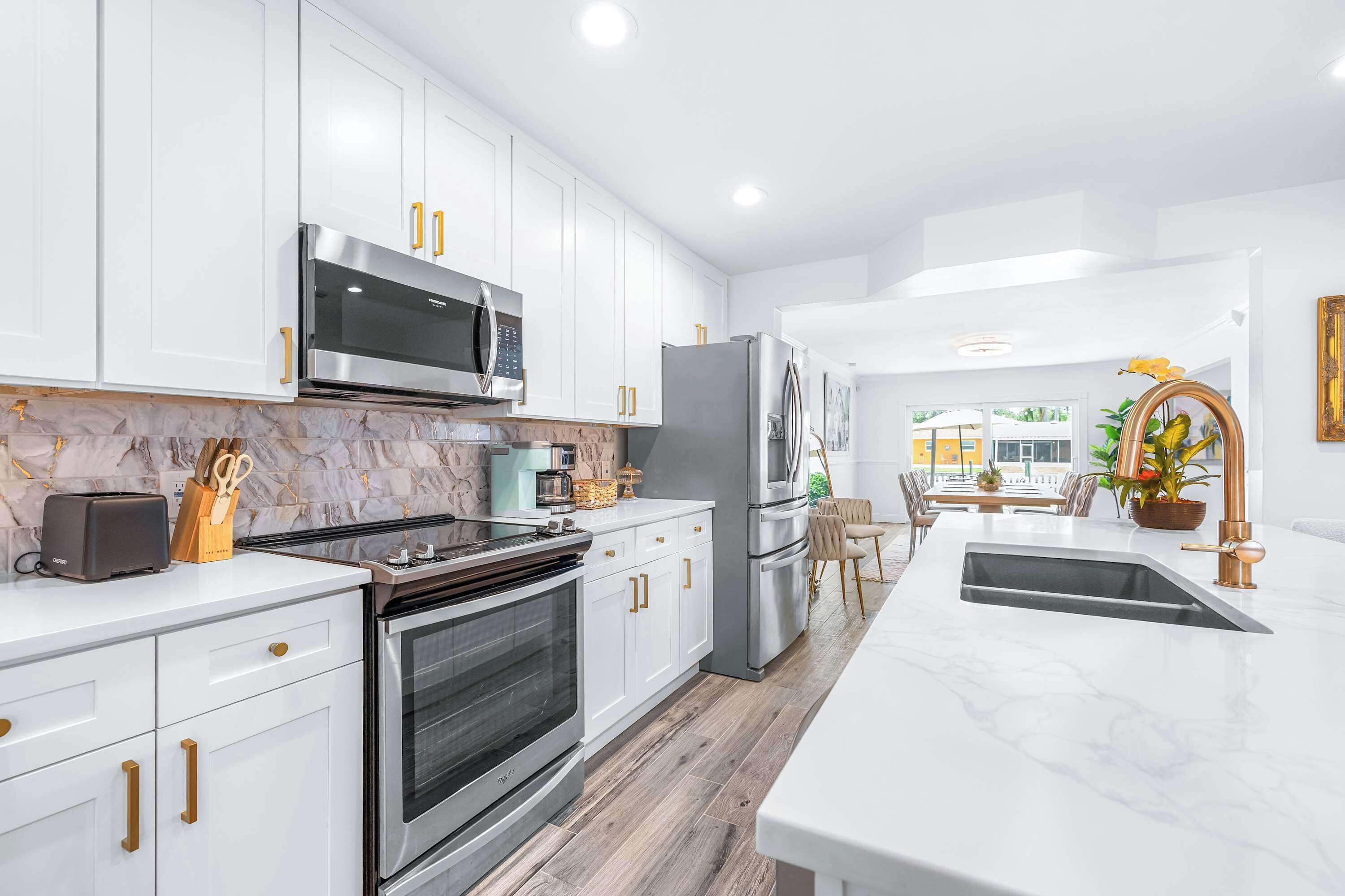Cocina moderna con armarios blancos, electrodomésticos de acero inoxidable y encimera de mármol.