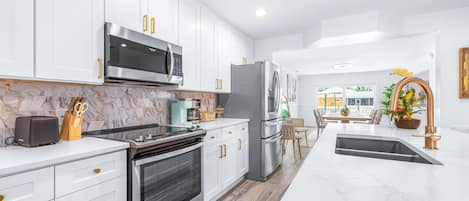A modern kitchen with white cabinetry, stainless steel appliances, and a marble countertop.