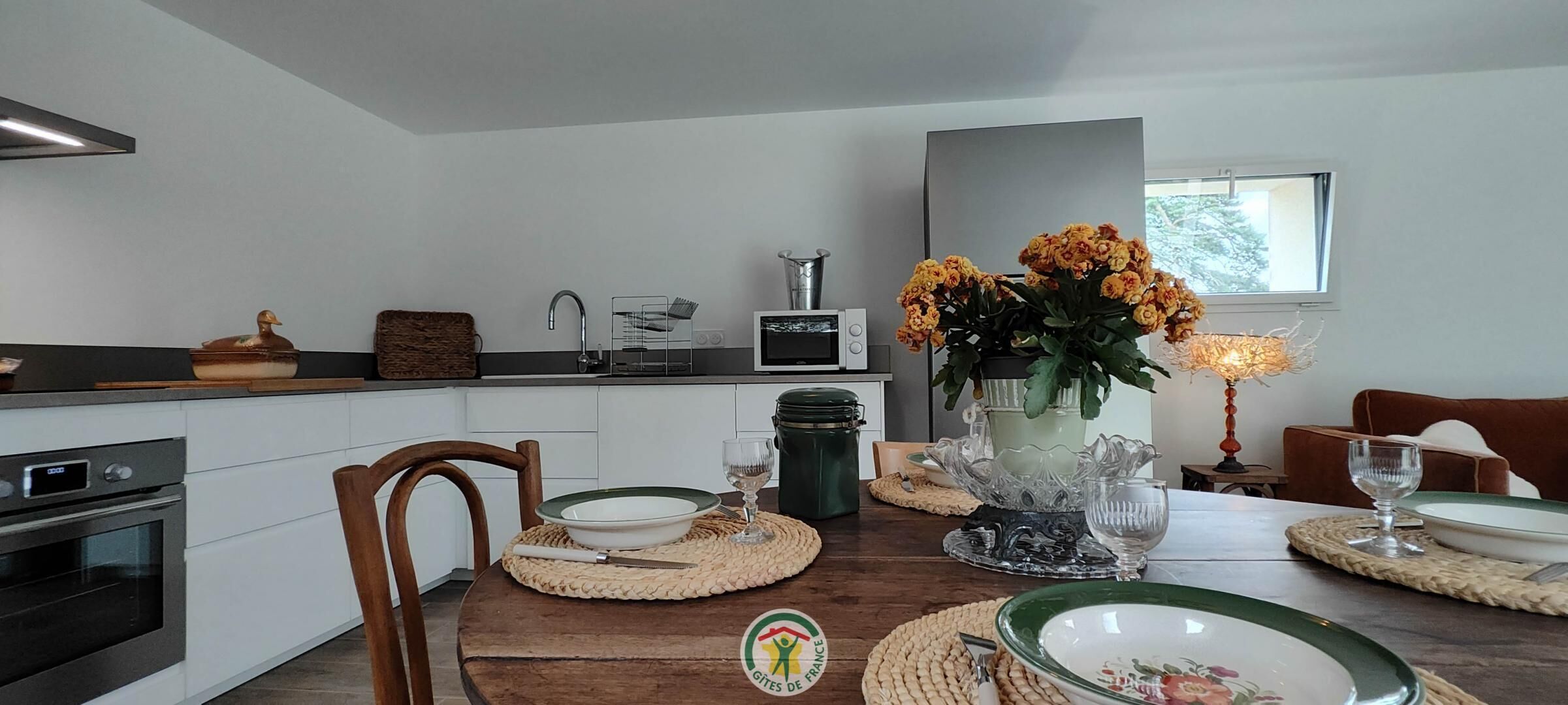 Une cuisine moderne avec des meubles blancs, un four à micro-ondes et un évier. On y trouve une table à manger ornée d'un vase de fleurs et de différents plats.
