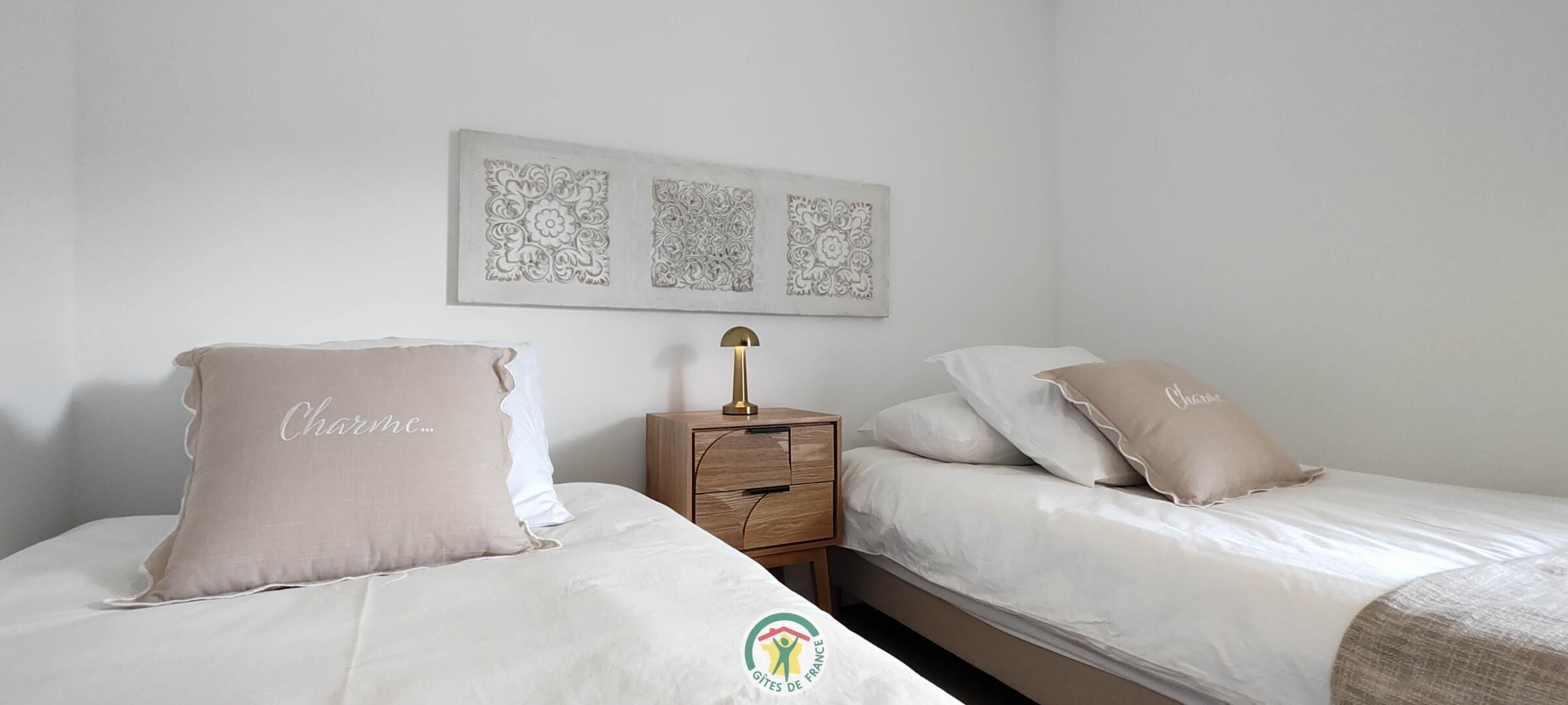 Une chambre avec deux lits, une table de chevet et des œuvres d’art décoratives au mur.