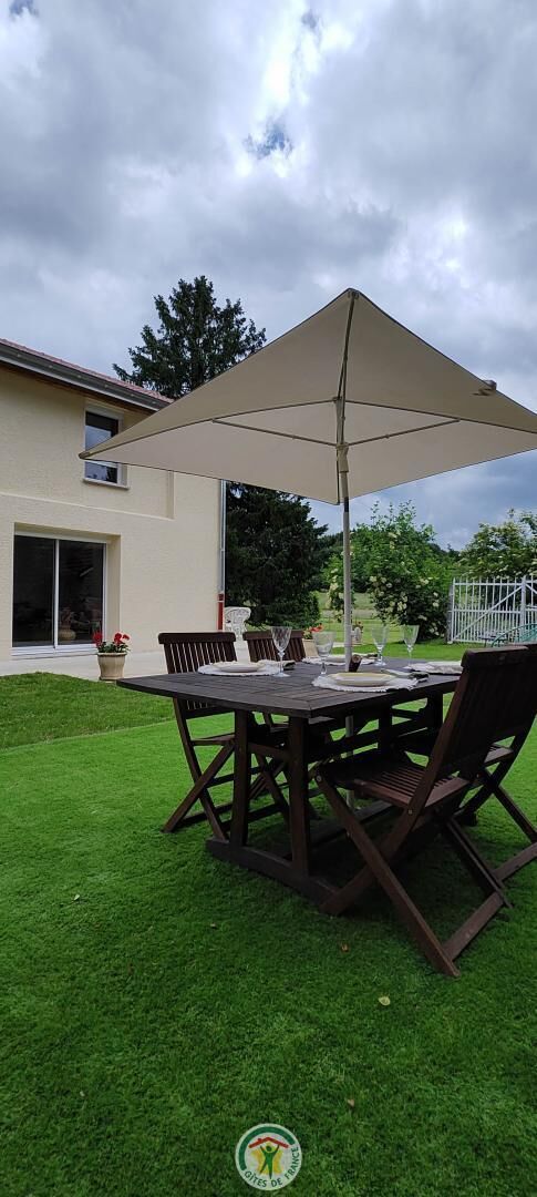 An outdoor patio with a table and chairs, a large umbrella, and a grassy lawn.