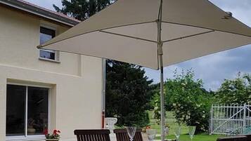 An outdoor patio with a table and chairs, a large umbrella, and a grassy lawn.