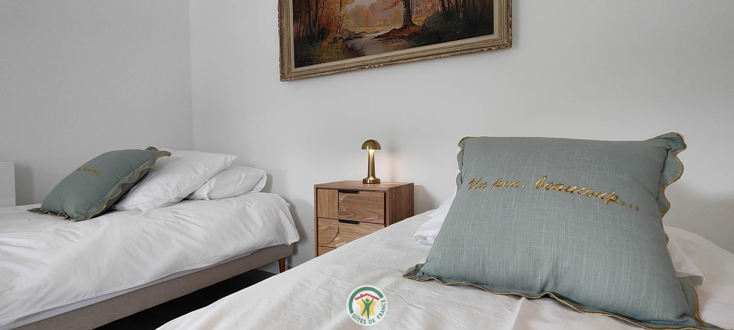 Una camera da letto con due letti, un comodino con una lampada e un quadro appeso al muro.