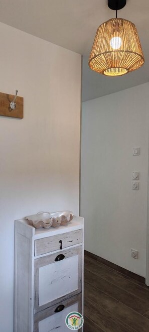 Una habitación con un aparador blanco, una lámpara de mimbre colgante y un adorno de madera en la pared.