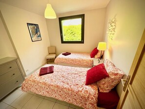 A bedroom with two beds, a chair, a dresser, a window with a view, and a wall-mounted lamp. - Lys Lodge - LE BOURG D'OISANS (LE BOURG D OISANS)