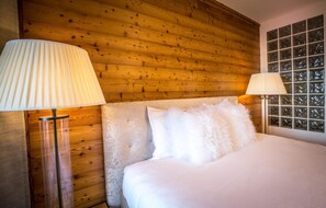 Habitación de hotel con cabecera de madera, dos lámparas de noche, un almohadón blanco mullido y una ventana con diseño de cuadrícula.