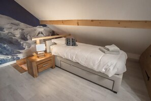 A bedroom with a bed, bedside table, lamp, and a wall mural. - THE VAUJANY MOUNTAIN LODGE (VAUJANY)
