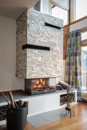 A stone fireplace with a glass front, logs, and a metal stand. - THE VAUJANY MOUNTAIN LODGE (VAUJANY)