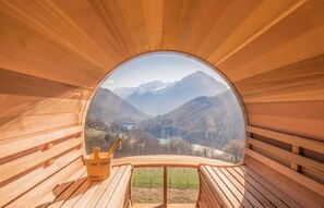 Interior de madera con un ventanal circular que ofrece vistas a un valle y montañas.