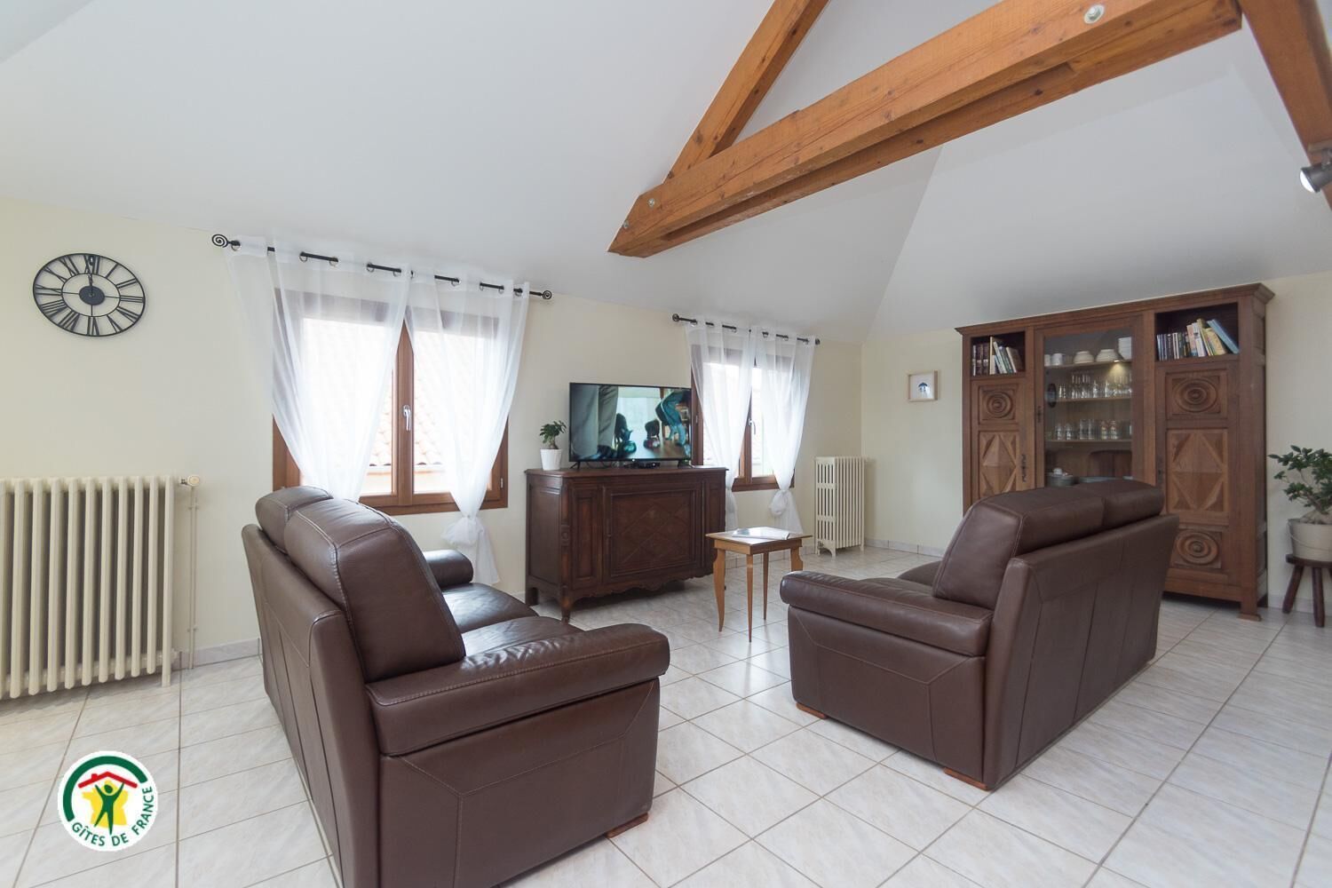 Un salon avec deux canapés en cuir marron, un meuble en bois doté de portes en verre, un téléviseur et un radiateur.
