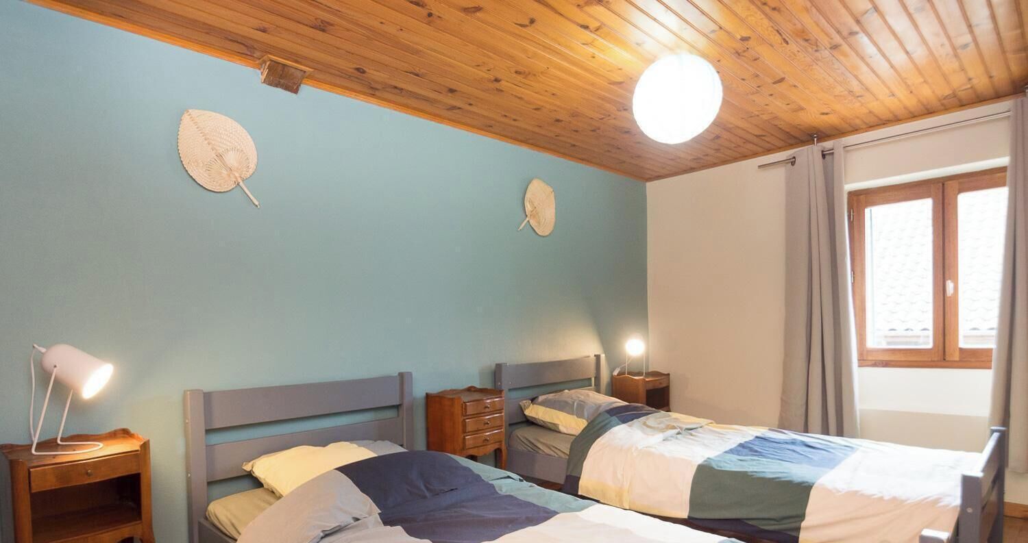 A room with two beds, wooden headboards, bedside tables, and a window with curtains.