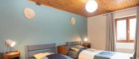 Ein Zimmer mit zwei Betten, Holz-Kopfteilen, Nachttischen und einem Fenster mit Vorhängen.