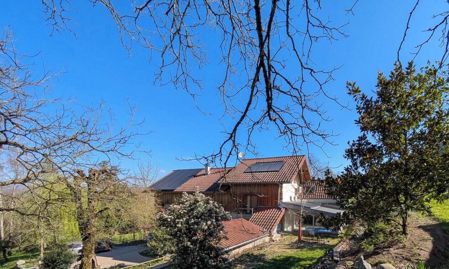 Une maison en bois à deux étages, avec un toit en pente, entourée d’arbres et surplombant un ciel bleu dégagé.