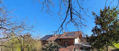Een houten huis met twee verdiepingen en een schuin dak, omringd door bomen en een helderblauwe lucht.