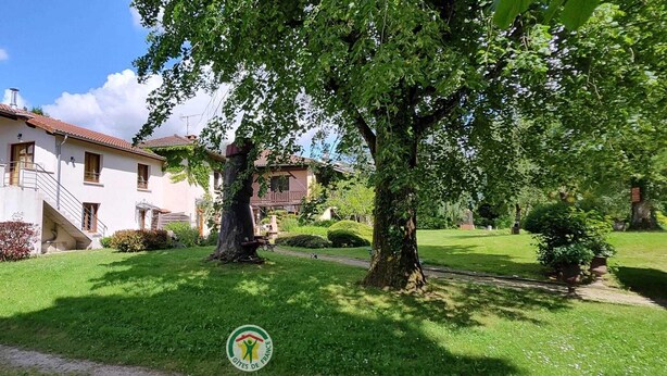 Una casa de dos pisos con balcón, rodeada por un césped cuidado y árboles.