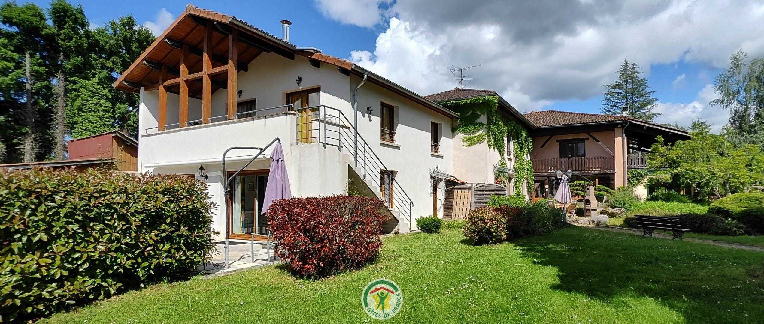 A two-story house with a wooden balcony, a staircase, and a well-maintained garden.