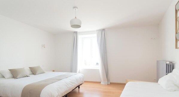 A bedroom with a bed, a bedside table, a radiator, and a window with curtains. - Domaine des Étoiles - La Villa Vacation Rental (GILLONNAY)
