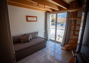 A room with a sofa, a framed picture on the wall, and a view through a glass door. - Maison La Blanche - 4**** (AUTRANS-MEAUDRE EN VERCORS)