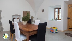 A dining area with a wooden table, white chairs, a potted plant, and a children's play mat.