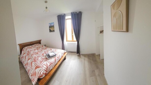 A bedroom with a bed, a window with curtains, a wall-mounted artwork, and a radiator.