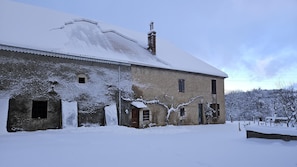 Edifici de dues plantes amb teulada coberta de neu i parets exteriors, amb una xemeneia, finestres i una porta.