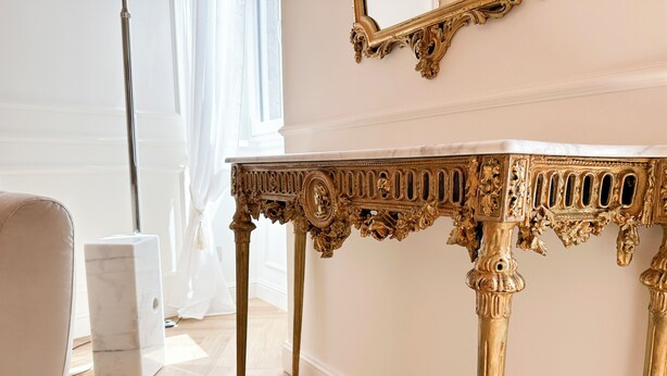 Une pièce avec un canapé blanc, une table en marbre ornée de motifs dorés et un grand miroir au mur.