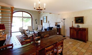 A dining area with a wooden table, chairs, and a chandelier. There is a sofa and a television in the background. - Gaillard Farm - LANS EN VERCORS (LANS EN VERCORS)