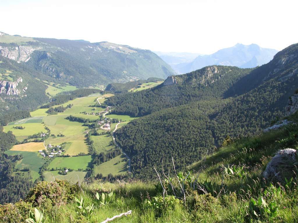 Un paisaje montañoso con un valle, una carretera sinuosa y edificios dispersos.