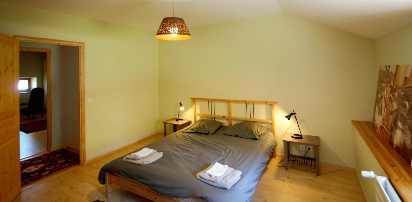 Un dormitorio con cama, lámparas de noche, cabecera de madera y una puerta que da a otra habitación.