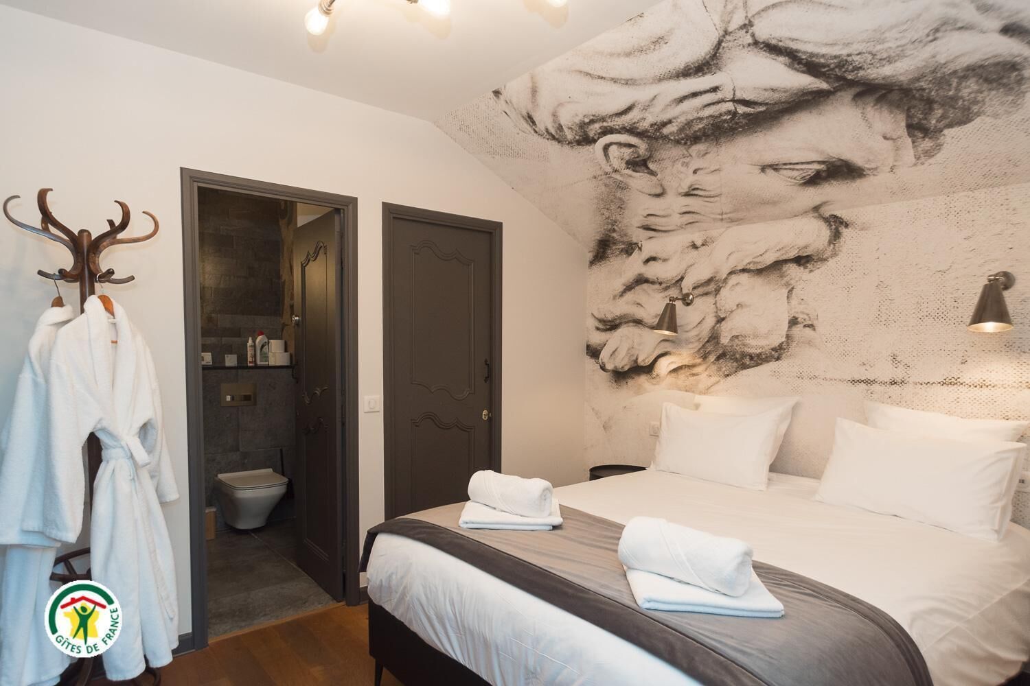 A bedroom with a large bed, a door leading to a bathroom, and a wall mural.