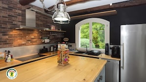Eine moderne Küche mit Backsteinwand, Holzbalken, einem Edelstahlkühlschrank und einem Fenster mit Blick ins Grüne.