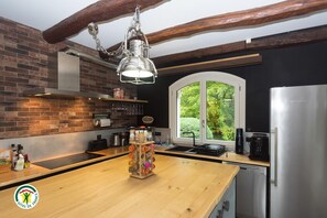 A modern kitchen with a brick wall, wooden beams, a stainless steel refrigerator, and a window with a view of greenery. - MY FATHER'S ESTATE - THE BEAUVOISIN BRIDGE (LE PONT DE BEAUVOISIN)