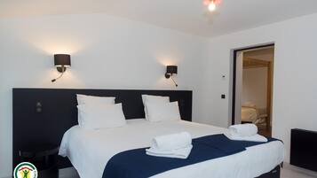 A modern hotel room with a large bed, two bedside lamps, a nightstand, and a visible door leading to another room.